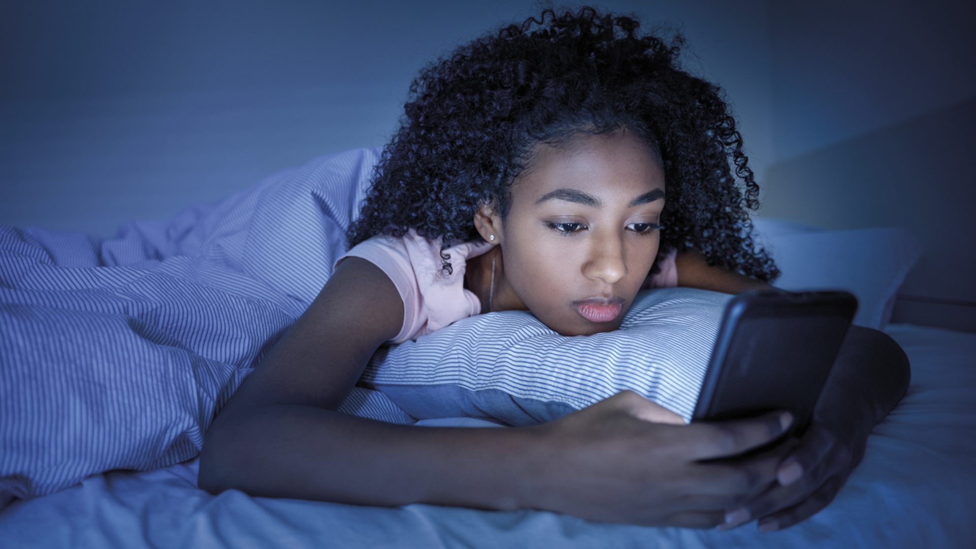 Black girl using smartphone in bed before sleeping